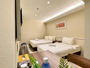 Habitación de hotel con dos camas, una mesa de madera, un hervidor, una botella y una obra de arte enmarcada en la pared.