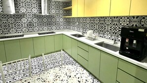 Une cuisine avec des meubles de couleur verte, un dosseret à motifs noir et blanc et une machine à café.