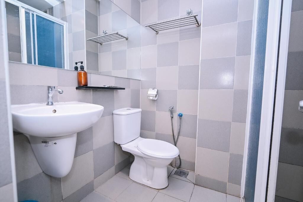 Et badeværelse med en hvid vask, toilet og bruser. Der er hylder over toilettet og et spejl over vasken.