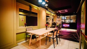 Een restaurantinterieur met een tafel en stoelen, een neonbord en een raam met een rood bord.