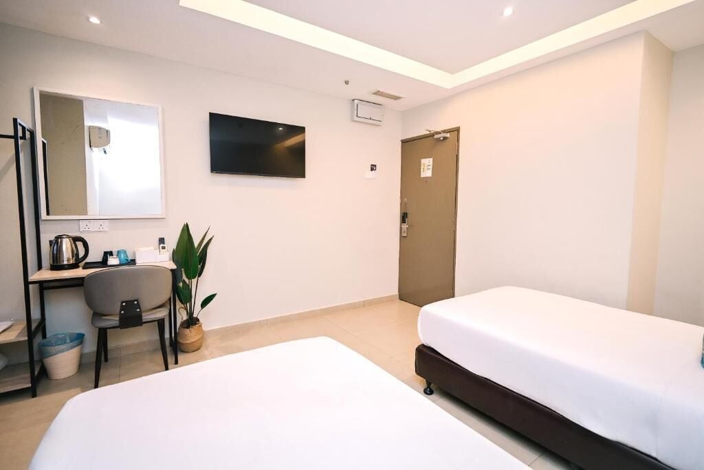 Une chambre d’hôtel avec deux lits, un bureau avec une chaise, une télévision et une porte.
