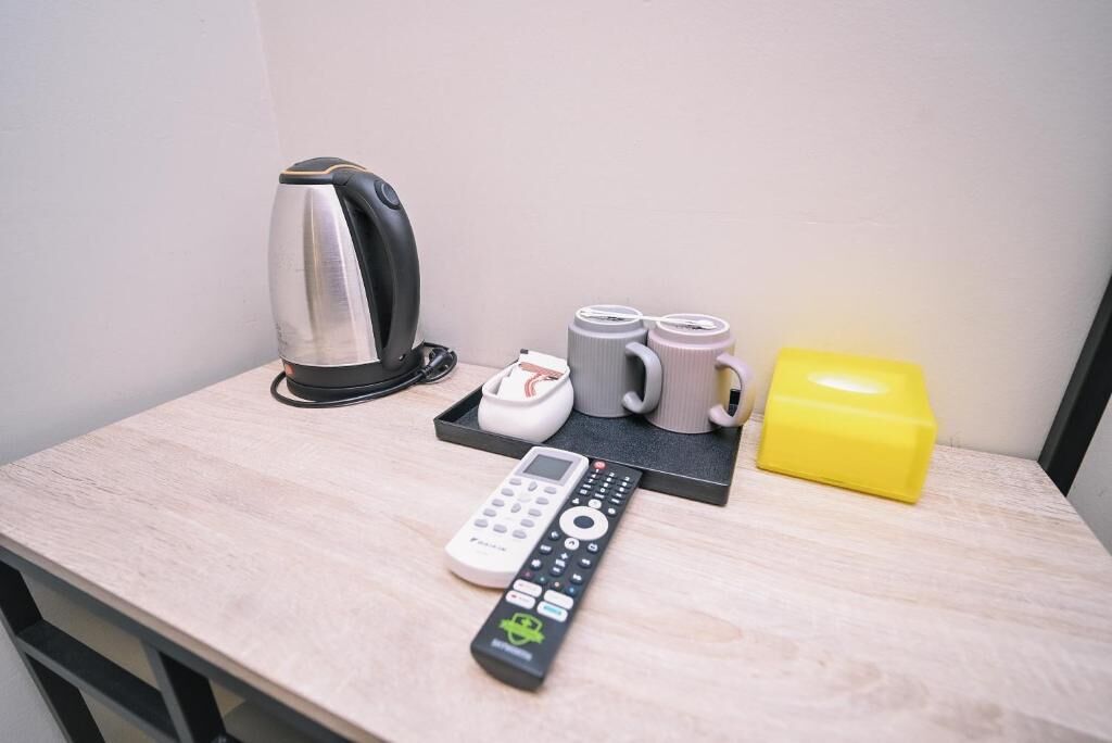A small table with a kettle, a phone, a remote control, and some mugs.