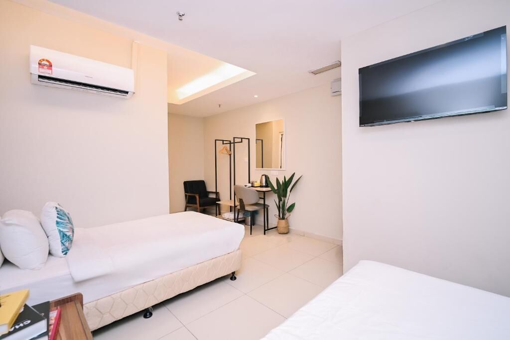 A hotel room with a bed, a desk, a chair, a TV, and an air conditioning unit.