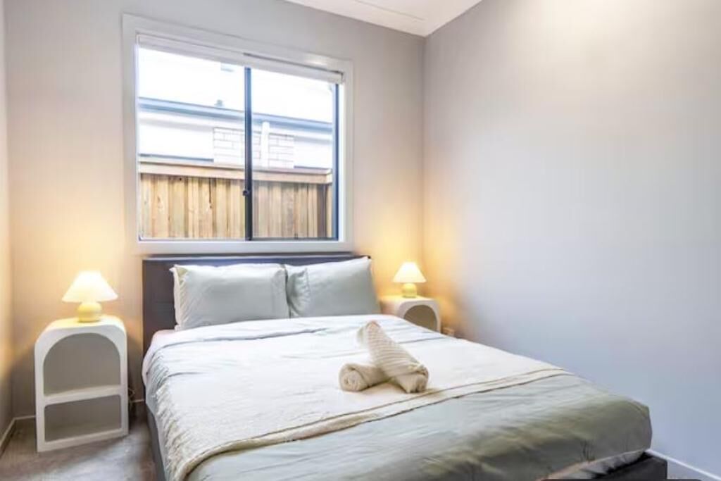 Een slaapkamer met een bed, twee bedlampen, een raam met jaloezieën en een handdoek op het bed.