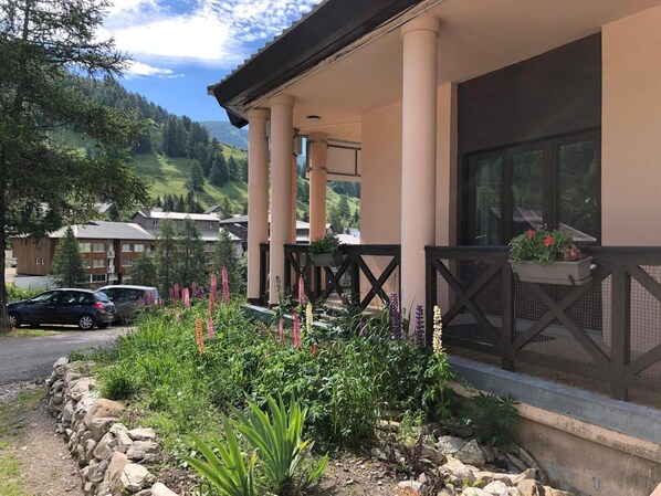 A hotel with a covered outdoor area, stone walls, and a variety of plants.
