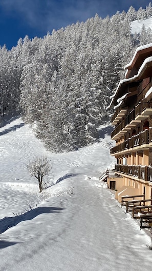 A snow-covered path leading to a building with balconies and a forest in the background.