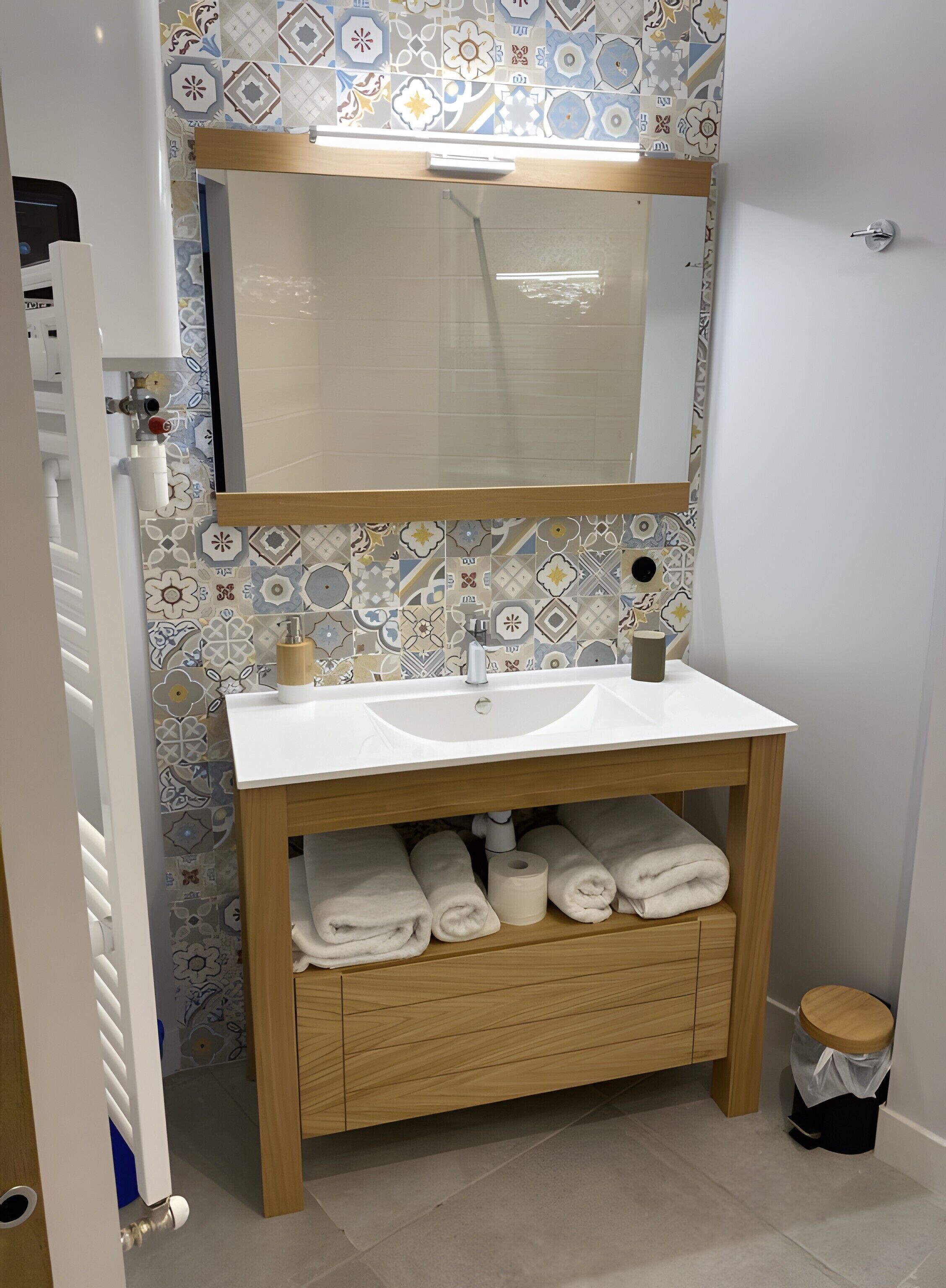 A bathroom with a white sink, wooden vanity, patterned tiles, a mirror, and a toilet.