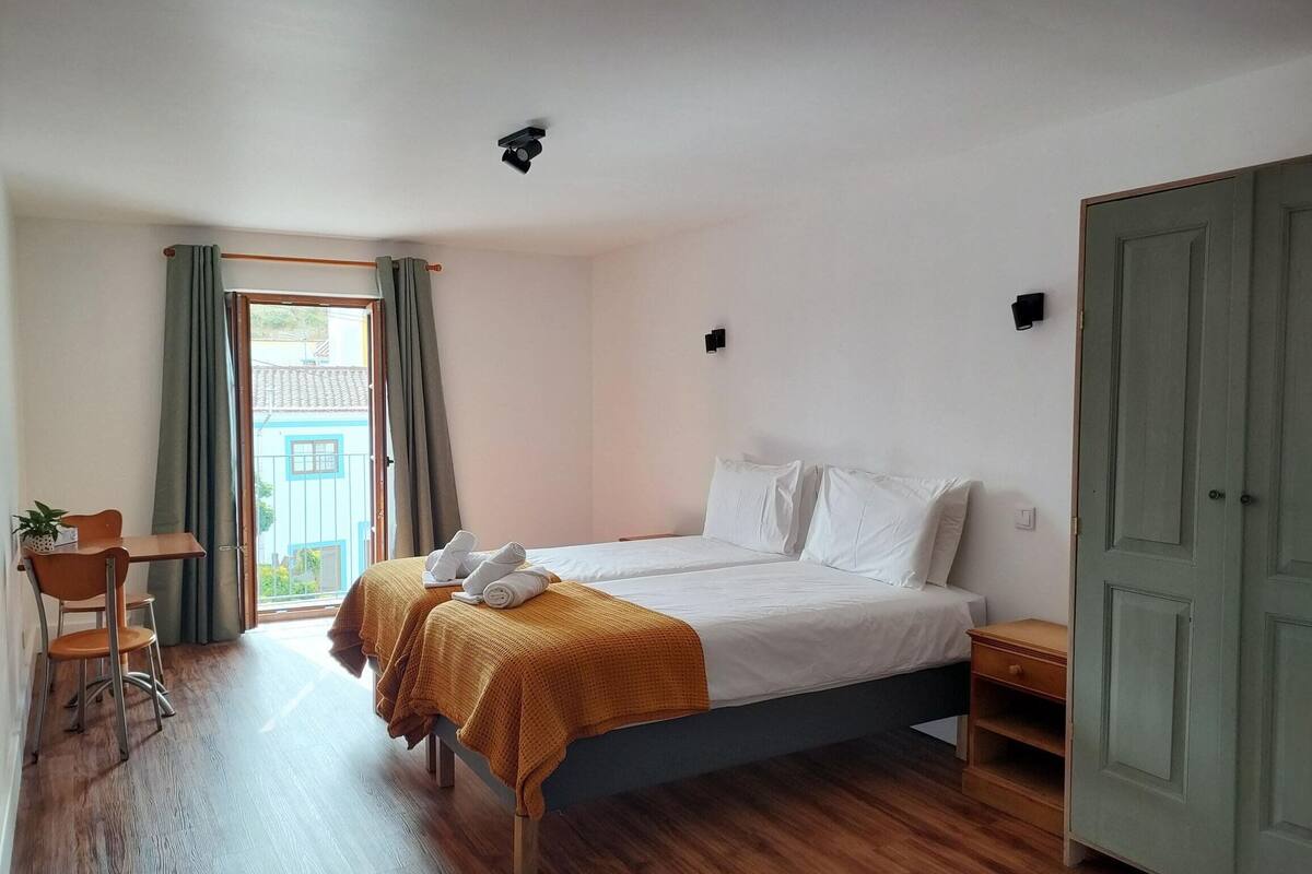 A bedroom with two beds, a wooden desk, a chair, and a wardrobe.