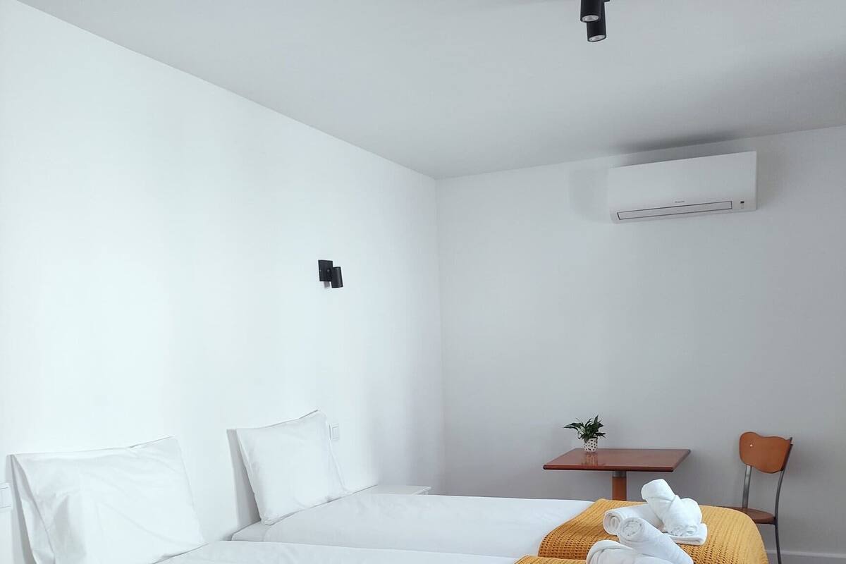 A modern hotel room with a large bed, a small table with a plant, and a chair.