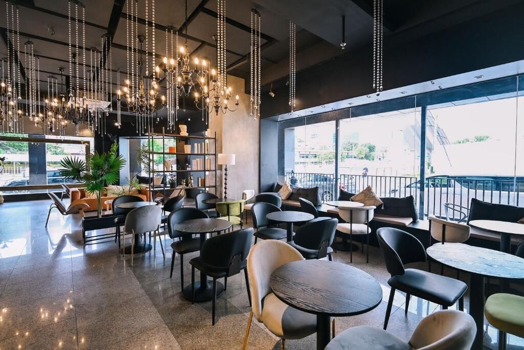 A modern cafe with multiple seating areas, including tables and chairs, and a large window offering a view of the outdoors.