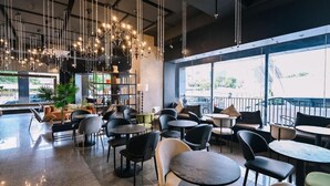 Een modern café met verschillende zithoeken, inclusief tafels en stoelen, en een groot raam met uitzicht op de omgeving.