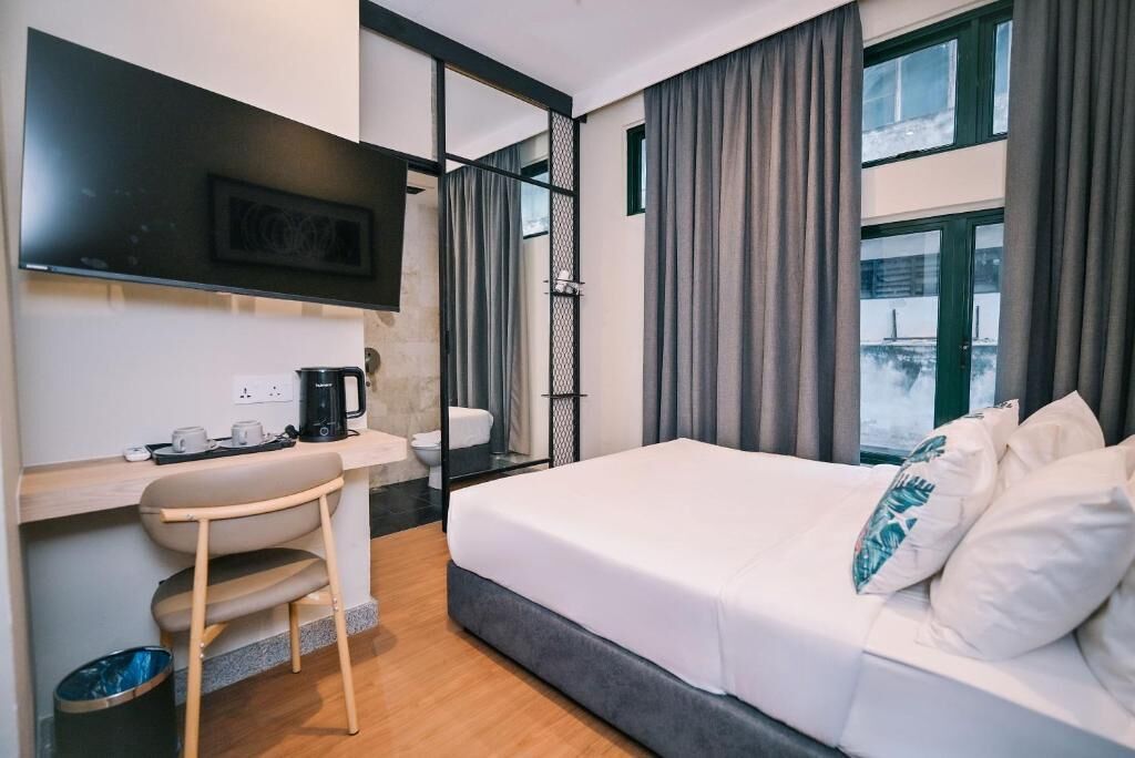 A modern hotel room with a bed, a desk with a coffee maker, a chair, and a large window with curtains.
