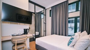 Een moderne hotelkamer met een bed, een bureau met koffiezetapparaat, een stoel en een groot raam met gordijnen.