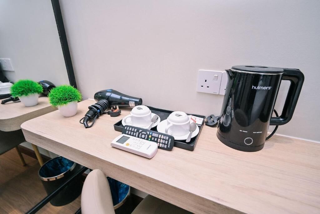 Et hotelværelse med et træskrivebord, en sort kaffemaskine, en vægt, to hvide kopper og to små krukker med planter.