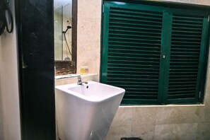 Een badkamer met een witte wastafel, een spiegel en een raam met groene luiken.