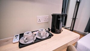 Een hotelkamer met een houten bureau, een zwarte koffiezetapparaat, twee witte bekers, een dienblad en een digitale thermometer.
