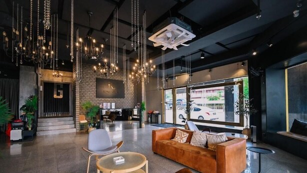 Een moderne lobby met een leren bank, ronde tafels, hangende lampen en een bakstenen muur.