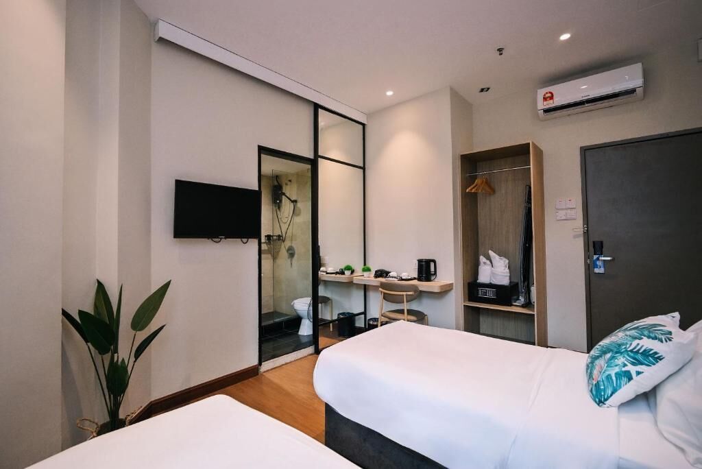 A hotel room with two beds, a TV, a shower area, a desk with a chair, and a wardrobe.