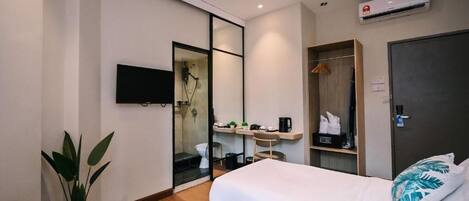 A hotel room with two beds, a TV, a shower area, a desk with a chair, and a wardrobe.