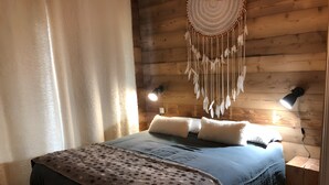 Habitación con paneles de madera, una cama, dos lámparas de pared y un adorno colgante de macramé.