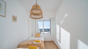 Een kamer met twee bedden, een groot raam en een hangende lamp van riet.