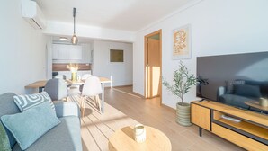 Een moderne woonkamer met een bank, salontafel, televisie en een eethoek met stoelen en een tafel.