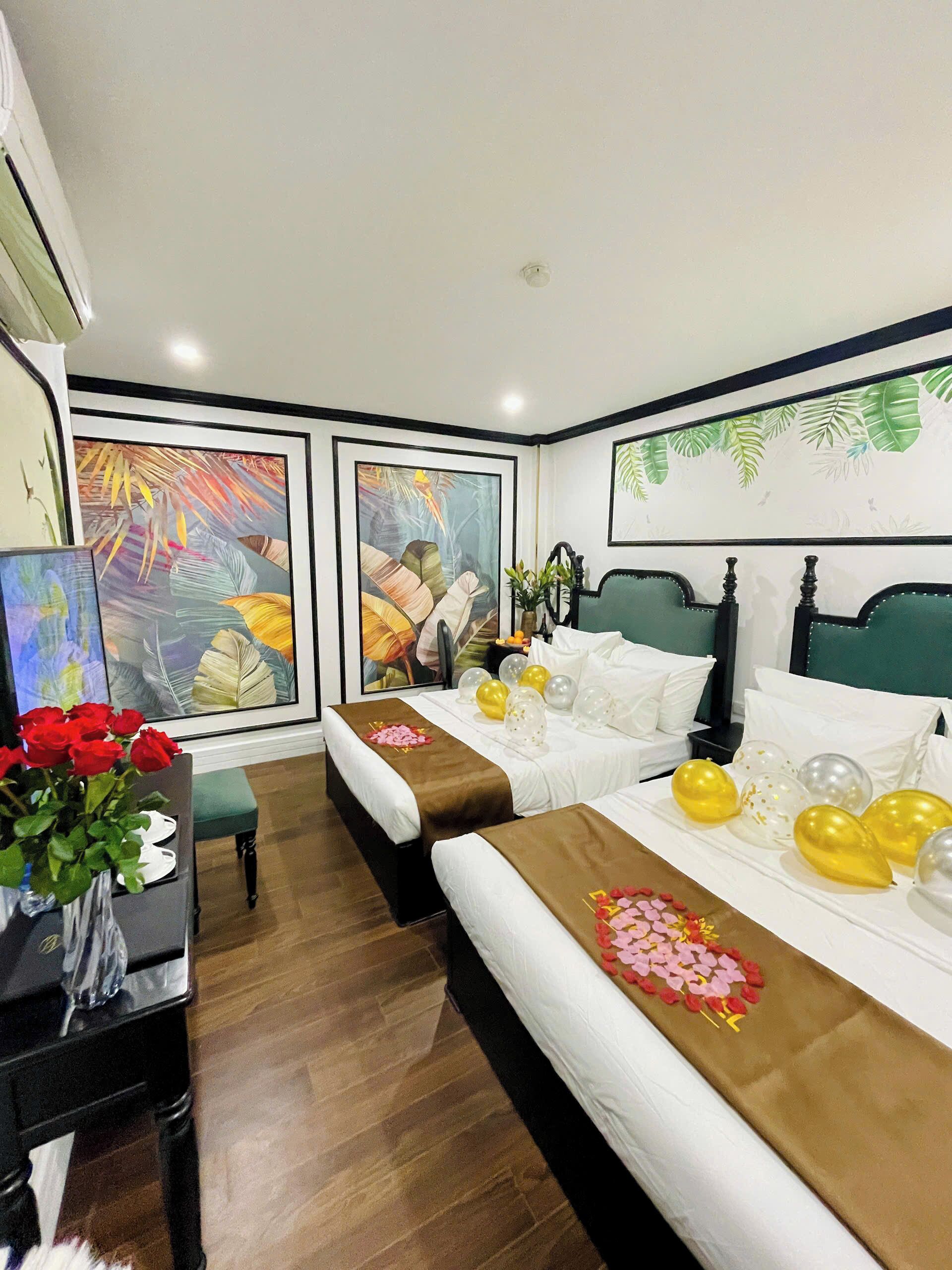 Habitación de hotel con dos camas, un escritorio y una jarra de rosas rojas, además de decoración de temática tropical.
