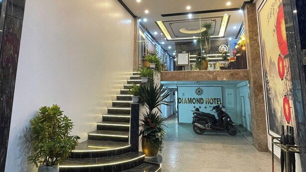 Un hall d’hôtel avec un escalier, une enseigne indiquant « Diamond Hotel », et une moto garée près de l’entrée.