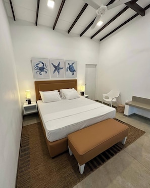 Quarto moderno com uma cama grande, cabeceira de madeira e ventilador de teto. Há duas luminárias fixadas na parede e uma mesinha de cabeceira.