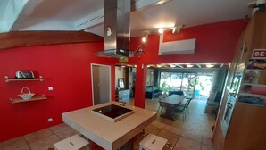 A kitchen with a central island, two stools, a refrigerator, and a dining area visible through an open door. - Beautiful modern villa with swimming pool in the heart of the garrigue (Lauret)