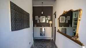 Un couloir avec un tapis à motifs, une armoire blanche dotée d’une porte en verre décorée, et un grand miroir avec un cadre doré.