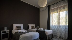Une chambre d’hôtel avec deux lits, une table de chevet, une lampe et une fenêtre avec des rideaux légers.