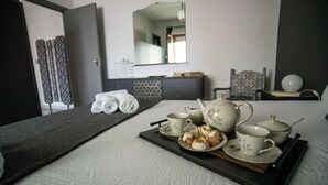 Un lit bien fait, avec un plateau contenant du thé et des pâtisseries, un miroir et une armoire, dans une chambre d’hôtel.