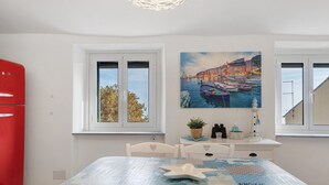 A room with a bed, a red appliance, a window with a view of trees, and a painting of boats on water. - Apartment 'Bedliving Nel Blu' with Sea View, Wi-Fi and Air Conditioning (Genova)
