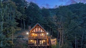 Een houten vakantiehuis met twee verdiepingen, met een balkon en terras, omringd door dicht bos.