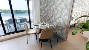 Een eetruimte met een ronde tafel voor vier personen, grote ramen met uitzicht op het strand en behangpapier met een patroon op de aangrenzende muur.