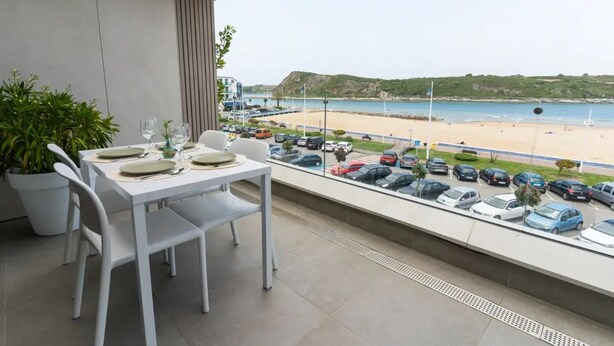 Een balkon met een tafel gedekt voor twee, met uitzicht op een parkeerplaats en strand.