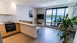 Een moderne keuken met een inbouwoven, een eethoek met tafel en stoelen, en een groot raam met uitzicht op zee.