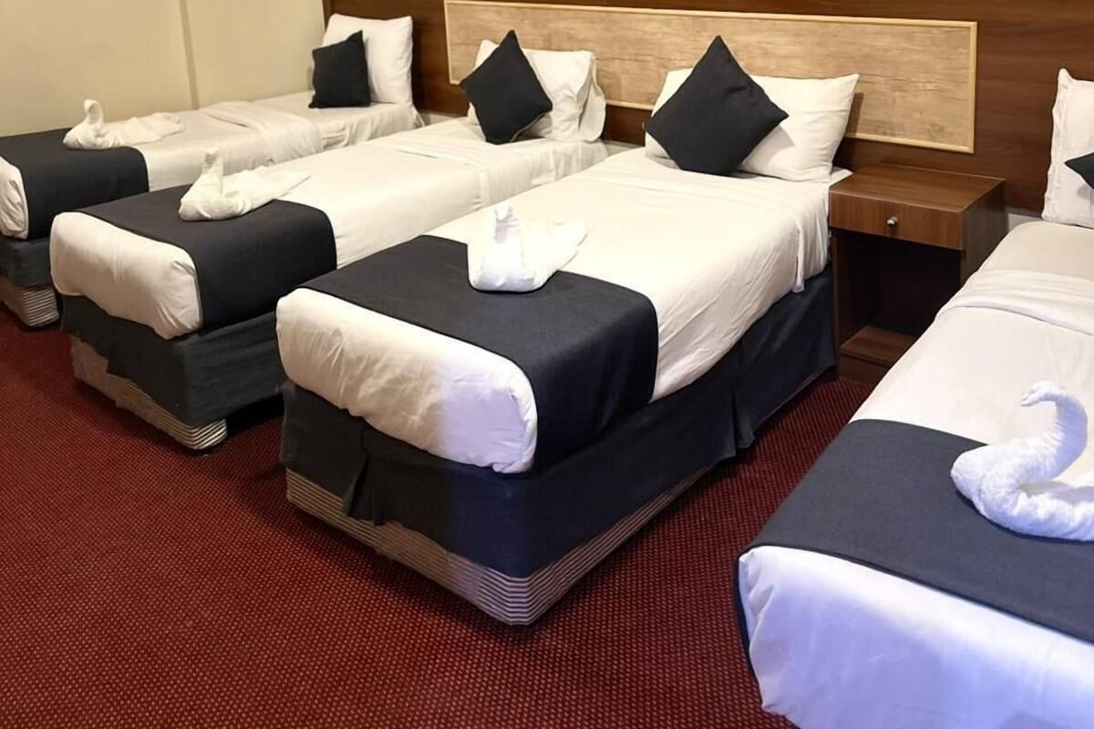 A hotel room with three beds arranged in a row, each with white linens and black headboards. The room features a patterned wallpaper with a floral design and a wooden headboard.