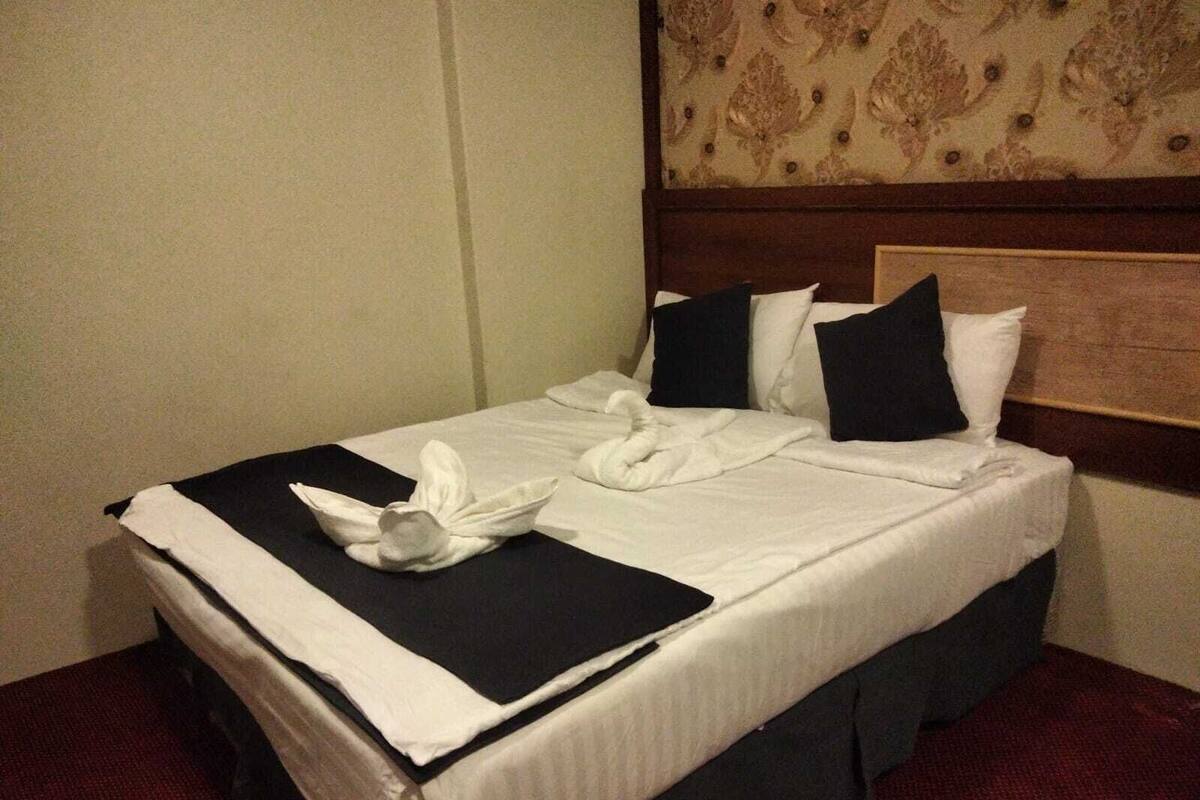 A neatly made bed with white linens, black and white pillows, and a folded towel on the bed.
