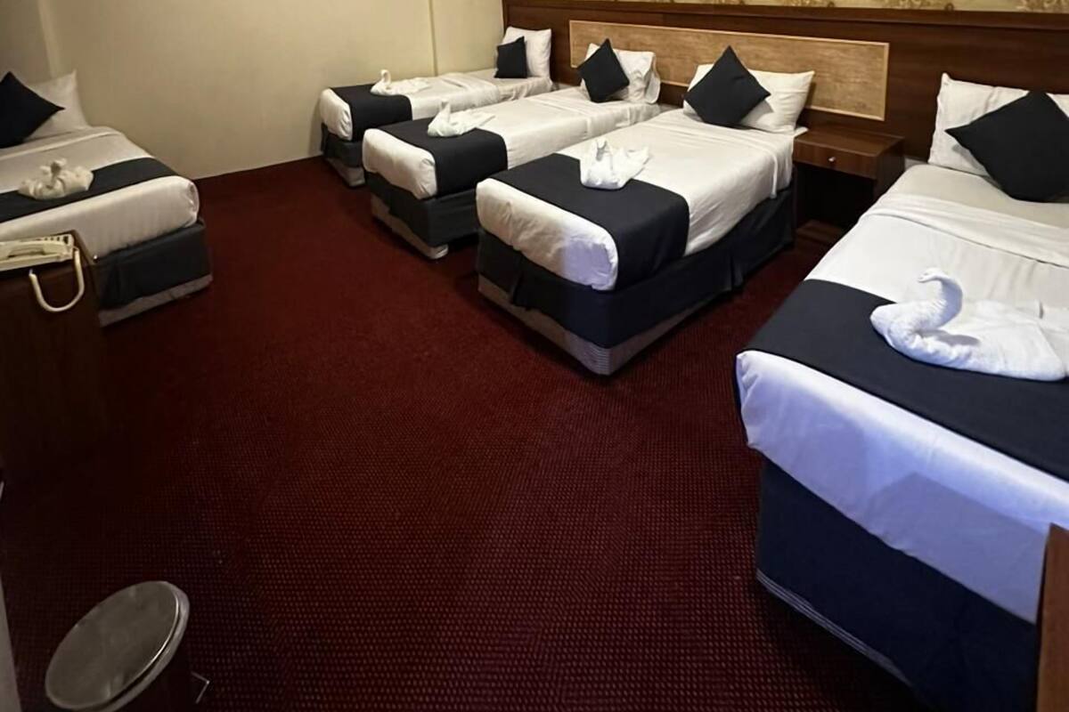 A hotel room with four beds arranged in a row, a wooden headboard, and a patterned wallpaper.