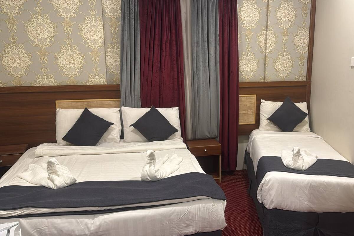A hotel room with two beds, each with a pillow and a towel. The room has a wooden headboard, a red carpet, and patterned wallpaper.