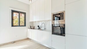 Ett modernt kök med vita skåp, en inbyggd ugn och ett fönster med utsikt över grönområden.