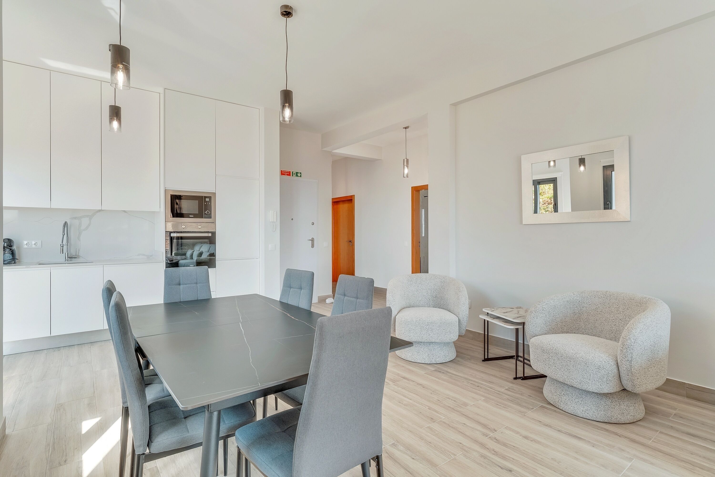 Una cocina moderna con armarios blancos, una mesa de comedor con sillas y un sillón grande.