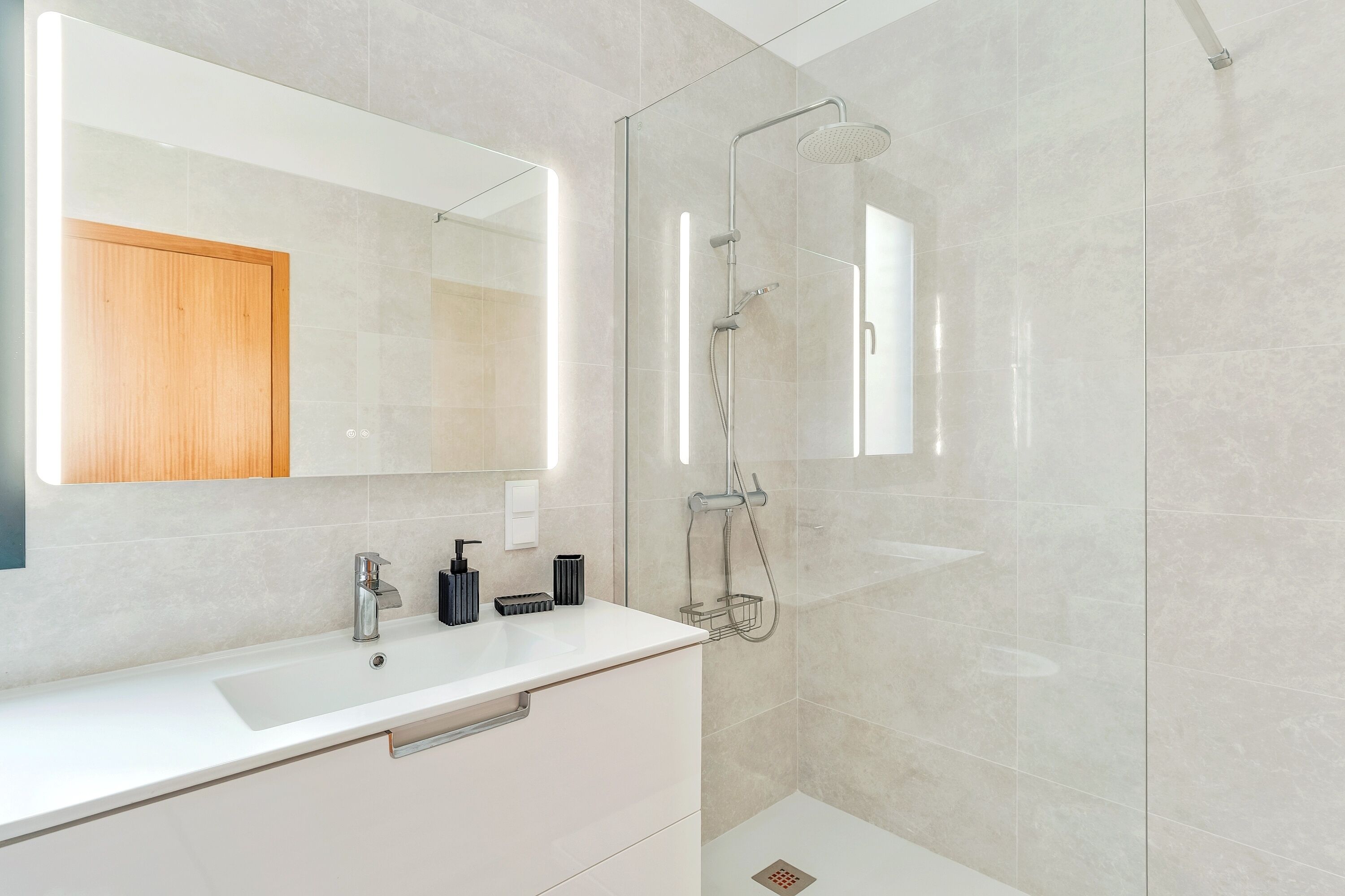 Ein modernes Badezimmer mit einer in Glas abgeschlossenen Dusche, einem weißen Waschbecken und einem Holzschrank.