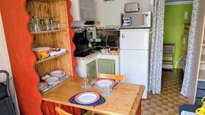 A compact kitchen with a refrigerator, microwave, and sink. There is a dining table set with plates and glasses. - Ground-floor Studio Cabin with terrace. Pets welcome! (leucate)