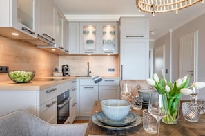 A modern kitchen with white cabinets, a wooden countertop, and a dining area with a table set for two. - Apartment 'Strandperle' with Sea View, Private Terrace and Wi-Fi (Glücksburg (Ostsee))