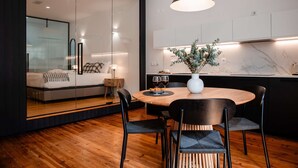 A modern bedroom with a glass partition, a wooden floor, and a dining area with a round table and chairs. - ✨Designer Loft with Balcony in Historic Baixa (Lisbon)