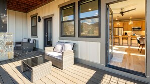 A covered outdoor seating area with wicker furniture and a glass door leading to a kitchen.