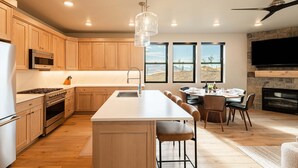 A modern kitchen with wooden cabinets, a central island, stainless steel appliances, and a dining area with a view.